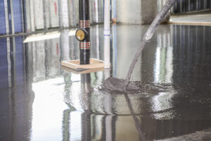 Liquid gypsum underlayment being pumped onto a subfloor around plumbing penetrations and structural framing.