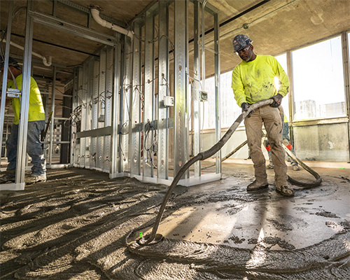 Commercial contractor pumping gypsum underlayment around steel stud framing on a multi-family building jobsite.